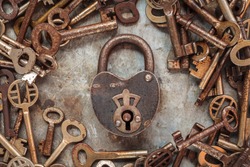 Vintage rusty padlock surrounded by old keys on a weathered steel background