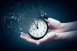 Concept of passing away, the clock breaks down into pieces. Hand holding analog clock with dispersion effect