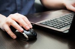 Human hand on computer mouse. Laptop on desk.