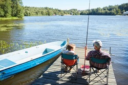 Father and son sitting on chairs on the pier and fishing together among beautiful nature