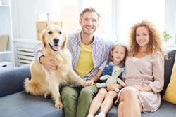 Happy and healthy family of mother, father, daughter and their cute pet sitting on sofa
