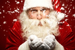 Photo of Santa Claus in eyeglasses blowing snow and looking at camera