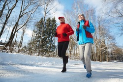 Happy active seniors in sportswear jogging down winter road in natural environment