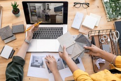 Contemporary designer pointing at home interior example on laptop display while consulting with colleague holding linoleum samples