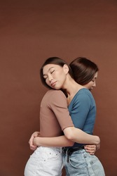 Two young beautiful female twins in casualwear standing in embrace with their eyes closed while expressing affection and love to one another