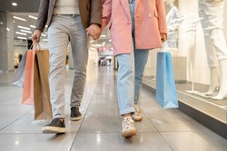 Close-p of young couple holding hands and walking together in shopping mall with purchases