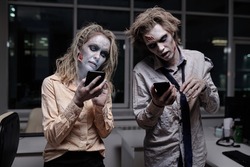 Dead and spooky businesspeople with zombie greasepaint on their faces and hands using smartphones