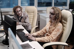 Gloomy businesswoman with zombie greesepaint using computer by desk