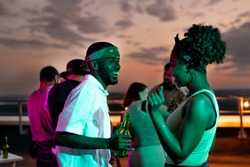 Happy young African couple dancing against their friends at rooftop party