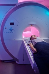 Young patient covered with blue towel undergoing medical examination in magnetic resonance imaging scan machine
