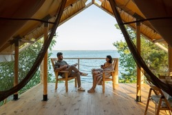Happy amorous couple relaxing in wooden armchairs on patio by glamping house
