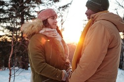Young amorous dates holding by hands on winter day while standing in front of camera