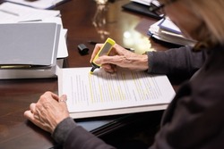 Hands of contemporary female lawyer with yellow highlighter underlining the main terms of contract or other juridical document