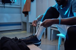 Young African soccer player tying shoelaces while sitting in changing room and getting ready for match or training