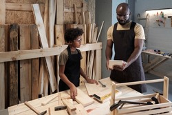 Portrait of African-American father teaching son carpentry while working together in woodworking shop