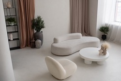 Part of large cozy and light living-room with white round table with handmade vases, comfortable sofa and armchair in apartment