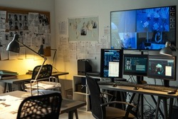 Corner of small office of FBI agency with set of criminal profiles hanging on board and large screen security camera on wall