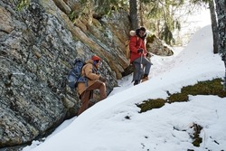 Young Black and Caucasian guys wearing backpacks hiking together in mountains on winter day, long shot