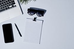 Flatlay of keyboard of laptop, stylish sunglasses, smartphone, pen and blank paper with clip with copyspace for your text on the right