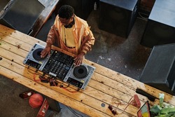 Above view of young African American male musician creating new music at lesire while touching turntables on dj set and mixing sounds
