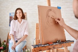 Hand of male artist drawing young woman on paper