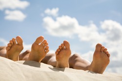 Image of soles of two people lying on sandy beach