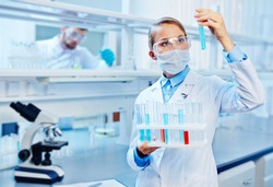 Young chemist analyzing liquids in lab on background of colleague