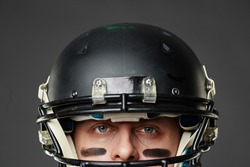 Isolated on black background closeup of head of blue-eyed man with eye black wearing football helmet and looking at camera prepared to face a challenge.