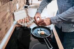 Man cooking eggs for breakfast, standing at the kitchen at home.