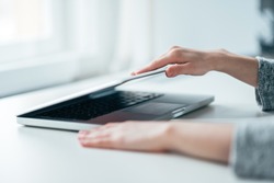 Close-up image of female hands open or close laptop on white table.