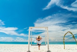 Young woman with hat on a swing in front of beautifull Indian Ocean tropical beach. Zanzibar vacation