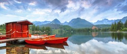Bright juicy red boats, landing near the bank of the clear blue lake, reflected in the water, with the romantic view on the big green Tatra Mountains
