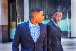 A young black businessman is standing by a mirror on the street and looking at the reflection. Concept of self assured, self esteem and self checking. A fine art lifestyle color photography.