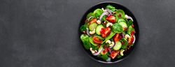 Spinach salad with fresh cucumbers, tomato, onion, pomegranate, sesame seeds and cashew nuts on black background. Healthy vegan food. Top view. Banner