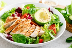 Grilled chicken meat and fresh vegetable salad of tomato, avocado, lettuce and spinach. Healthy and detox food concept. Ketogenic diet. Buddha bowl dish on white background