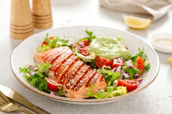 Grilled salmon fish fillet and fresh green lettuce vegetable tomato salad with avocado guacamole.