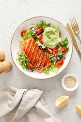 Grilled salmon fish fillet and fresh green lettuce vegetable tomato salad with avocado guacamole. Top view.