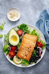 Grilled salmon fish fillet and fresh vegetable salad with tomato, red onion, black olives and avocado