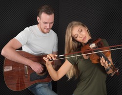 Portrait of a handsome man musician plays the guitar, a beautiful woman musician plays the violin in the recording studio.