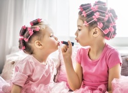 Happy childhood. Two sisters are doing hair and having fun. Children doing makeup sitting on the bed in the bedroom.