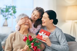 Happy women's day! Child daughter is congratulating mom and granny giving them flowers tulips. Grandma, mum and girl smiling and hugging. Family holiday and togetherness.