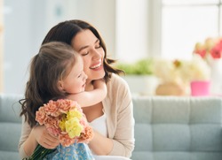 Happy mother's day! Child daughter congratulates mom and gives her flowers. Mum and girl smiling and hugging. Family holiday and togetherness.                               
