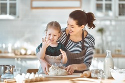 Happy loving family are preparing bakery together. Mother and child daughter girl are cooking cookies and having fun in the kitchen. Homemade food and little helper.                                  