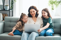 Happy loving family. Young mother and daughters girls using laptop. Funny mom and lovely children are having fun staying at home.                               