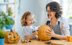 Happy family preparing for Halloween. Mother and child carving pumpkins at home. 