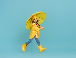 Happy emotional child laughing and jumping. Kid with yellow umbrella on colored teal background.