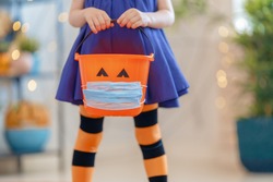 Happy Halloween! Little kid with a basket for sweets  wearing face mask protecting from COVID-19.