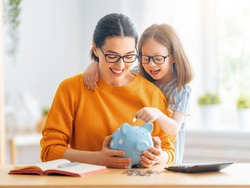 Woman and child sitting at desk with a piggy bank are calculating expenses, managing the family budget.