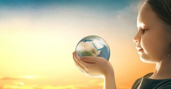 Child is holding planet in hands on sunset sky background. Earth day holiday concept.