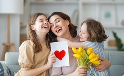 Happy mother's day. Children daughters are congratulating mom and giving her flowers. Mum and girls smiling and hugging. Family holiday and togetherness.